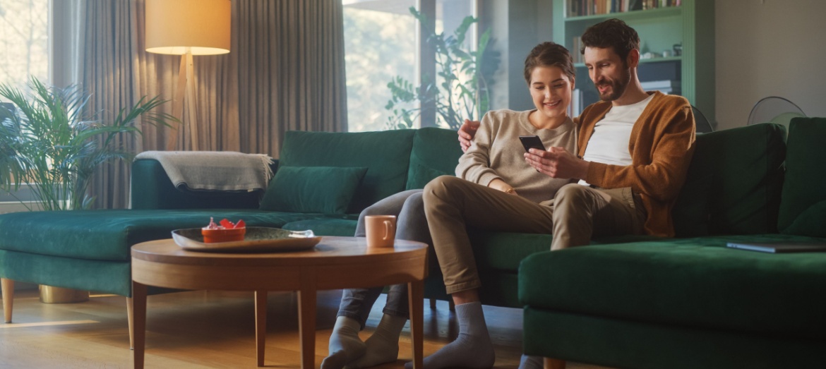 A couple sitting on the sofa together and using a phone.