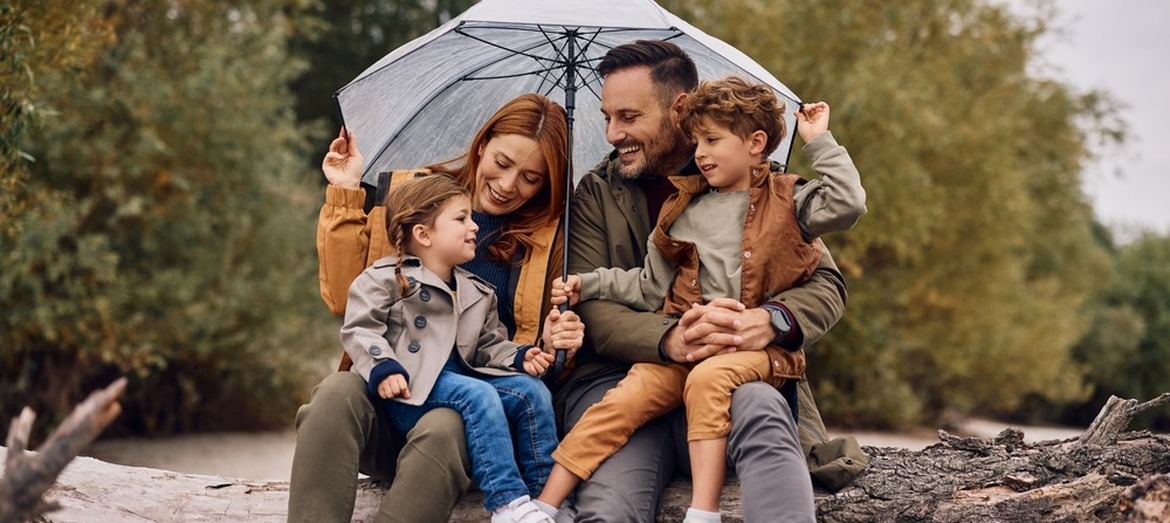 A young family sheltering under an umbrella and smiling.