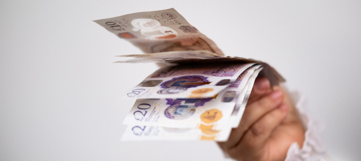 A hand holding UK bank notes.