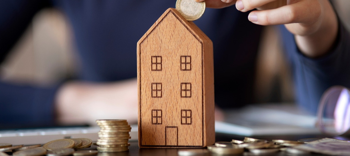A person placing coins into a moneybox shaped like a house.